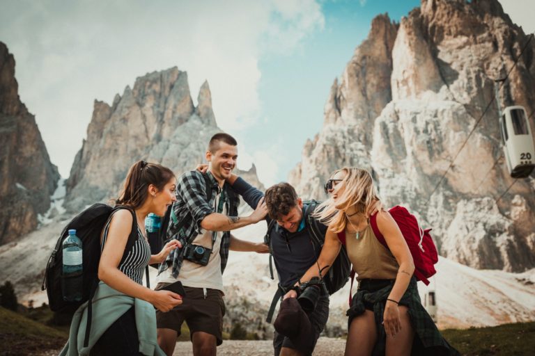 A group of four student travelers joke around with the mountains in the background at the Dolomite Alps, Italy.