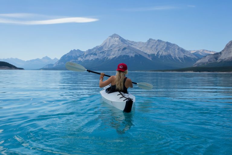 A female student traveler taking a kayak tour with mountains in the distance on a lake in Nordegg, Alberta, Canada.