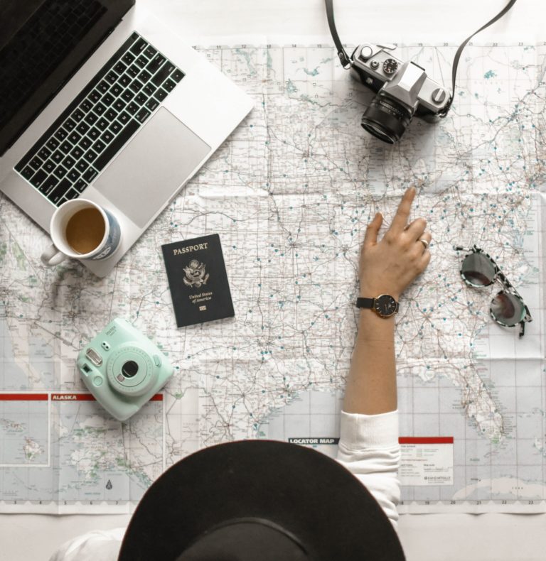 A student traveler pointing on a map with travel accessories surrounding her.