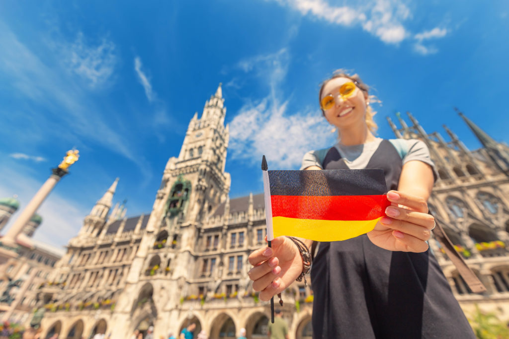 A happy female student with a German flag poses against the background of the city hall in Munich. She is studying abroad on a educational vacation from her college with Students Fare.