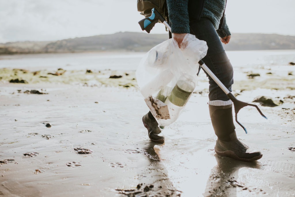 A volunteer walking on the beach holding a garbage bag of trash to help a beach cleanup. This is a young adult student traveling for education on a study abroad vacation.