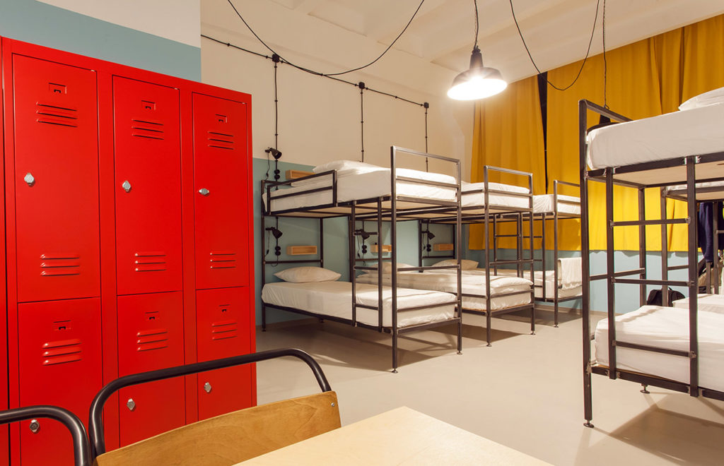 The interior of a modern hostel for cheap accommodations so student travelers can save money on their study abroad programs. In the corner are tall red lockers, which Students Fare recommends that your hostels always have.