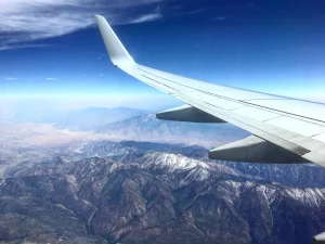 A flight with Students Fare looking out the airplane window at the wing and the mountains below.