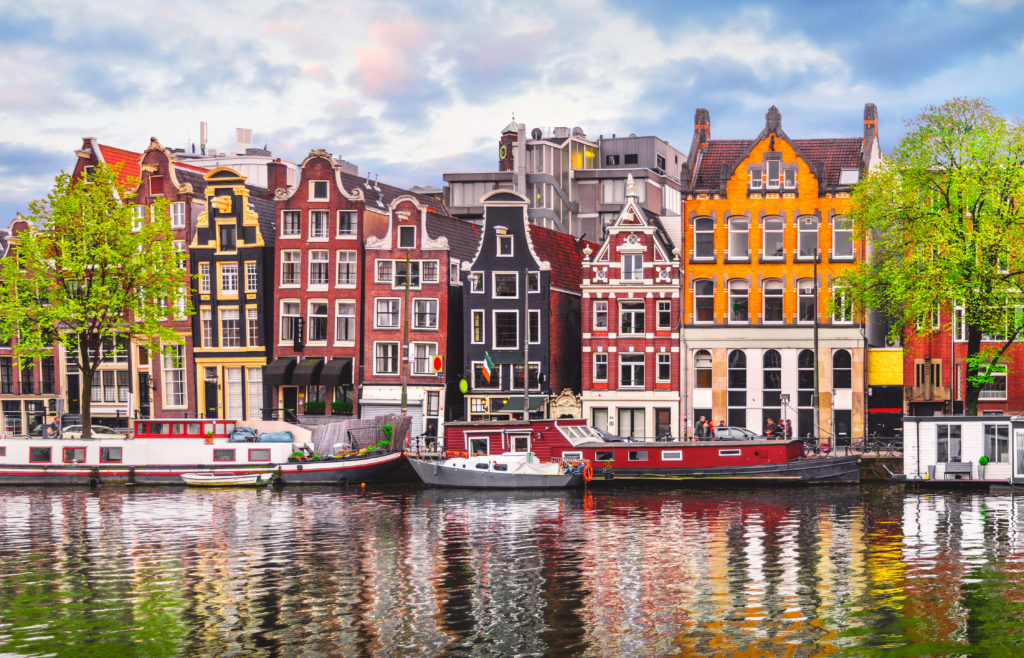 A travel photo of a river in Amsterdam, Netherlands with boats and beautiful apartment houses. The image is featured in the Students Fare article about college students called top fall break destinations.