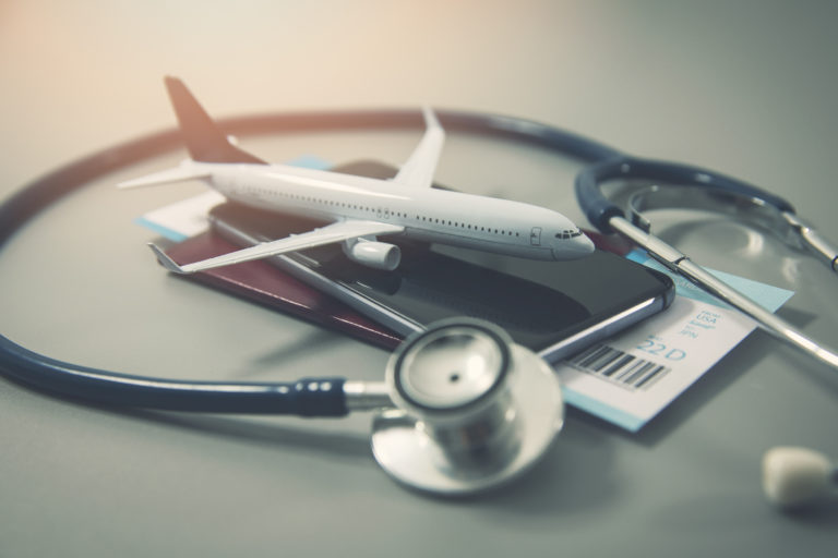 An image demonstrating the concept of travel insurance, with a small airplane sitting on an airline ticket and passport, surrounded by a large stethoscope. This image is used in the Students Fare travel blog, "the ultimate travel insurance 101 guide," which describes travel insurance, its importance, and the various insurance options available.