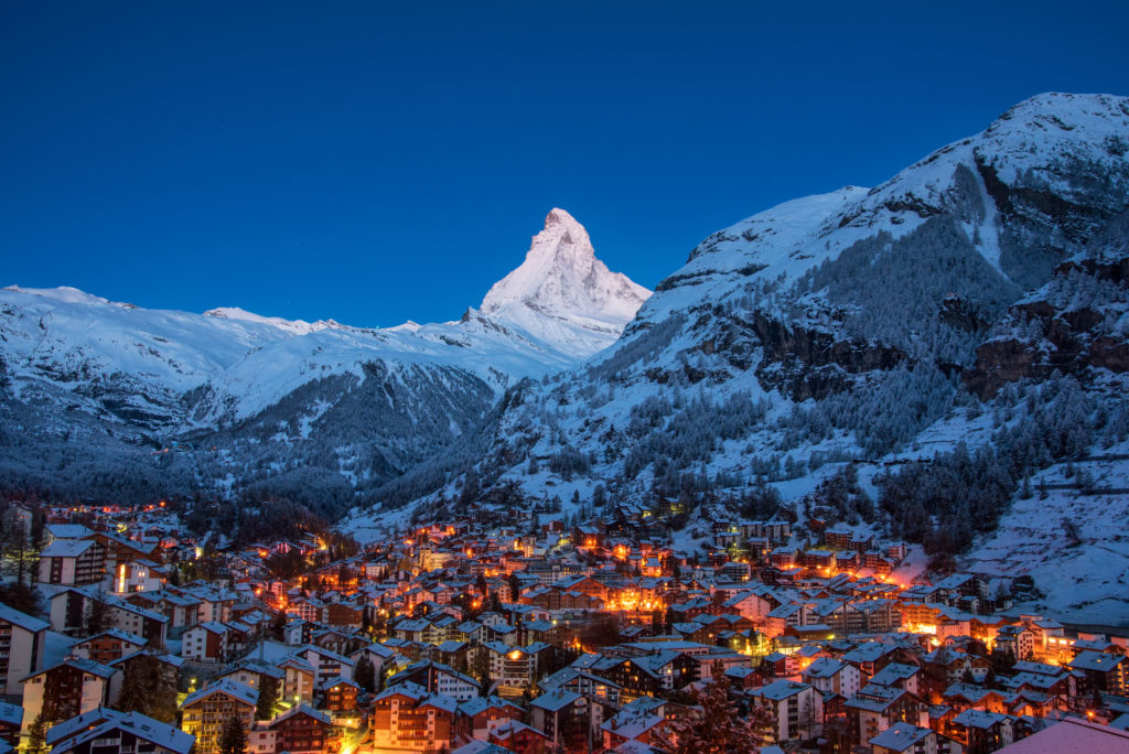 The late night landscape view from Zermatt City Village in Switzerland, with a small town lit up with lights in the valley. This image is used in the Students Fare student travel blog, "Spring Break in Switzerland," which is a travel guide to celebrating spring vacation in the Swiss Alps.