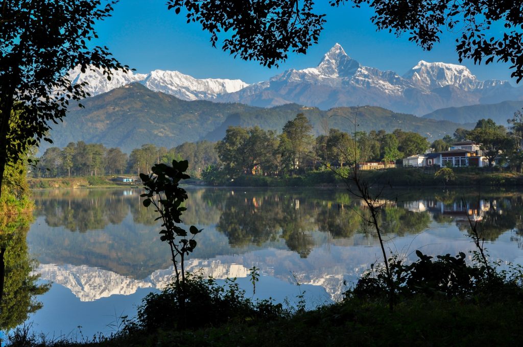 A beautiful mountain in Pokhara, Nepal covered in snow in the background of the image is reflected in a large lake in the foreground. This image is used in the Students Fare student travel blog, "Best Paragliding Destinations," which is a travel guide for paragliding all around the world.