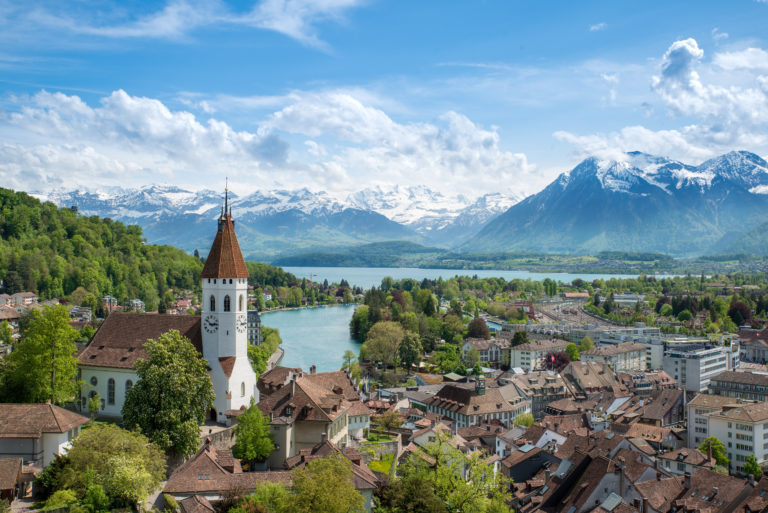 A landscape shot of the historic city of Thun in the canton of Bern in Switzerland, with a folk town below the mountains and blue lake. This image is used in the Students Fare student travel blog, "Spring Break in Switzerland," which is a travel guide to celebrating spring vacation in the Swiss Alps.