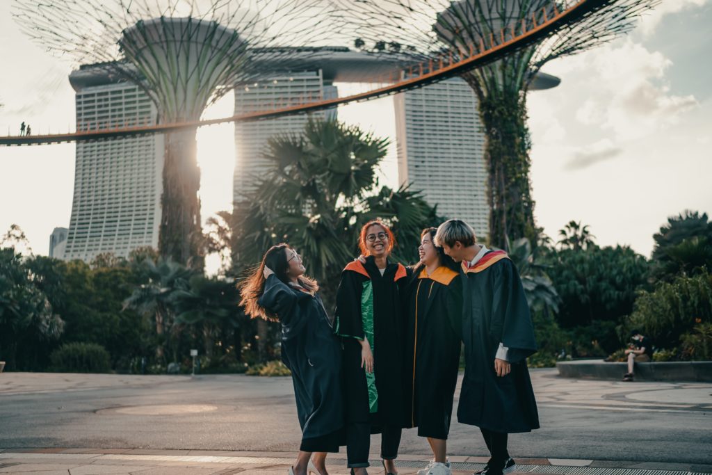 A group of four university students in their graduation gowns celebrating under beautiful architecture. The featured image in the Students Fare student travel blog, "Best College Towns in America," which describes the top university cities in the USA.