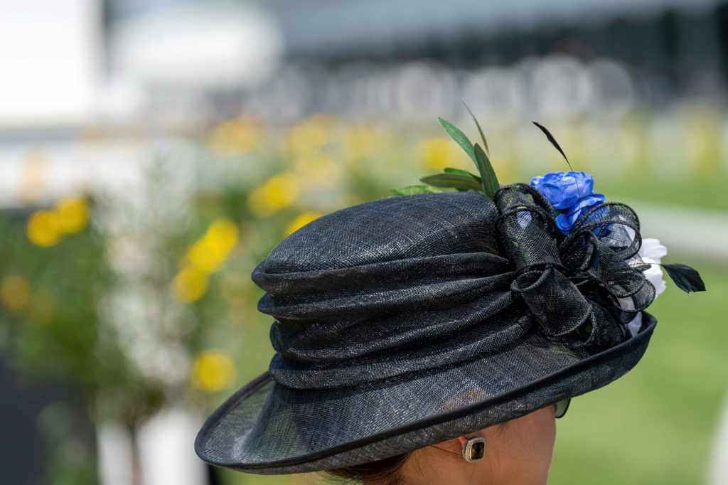 A photo of a woman shot from behind at the Kentucky Derby in Louisville, Kentucky where she wears a large black hat with a bow, feathers, and blue and white flowers. This image is used in the Students Fare student travel blog to list the top spring break destinations for college students in 2023!