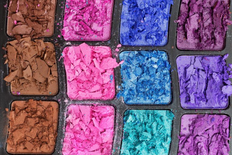 A closeup of an eyeshadow makeup pallet with the colored pigment broken from the rough flight. This image is used in the Students Fare student travel blog to share tips for packing luggage, "a guide to traveling with makeup and toiletries!"