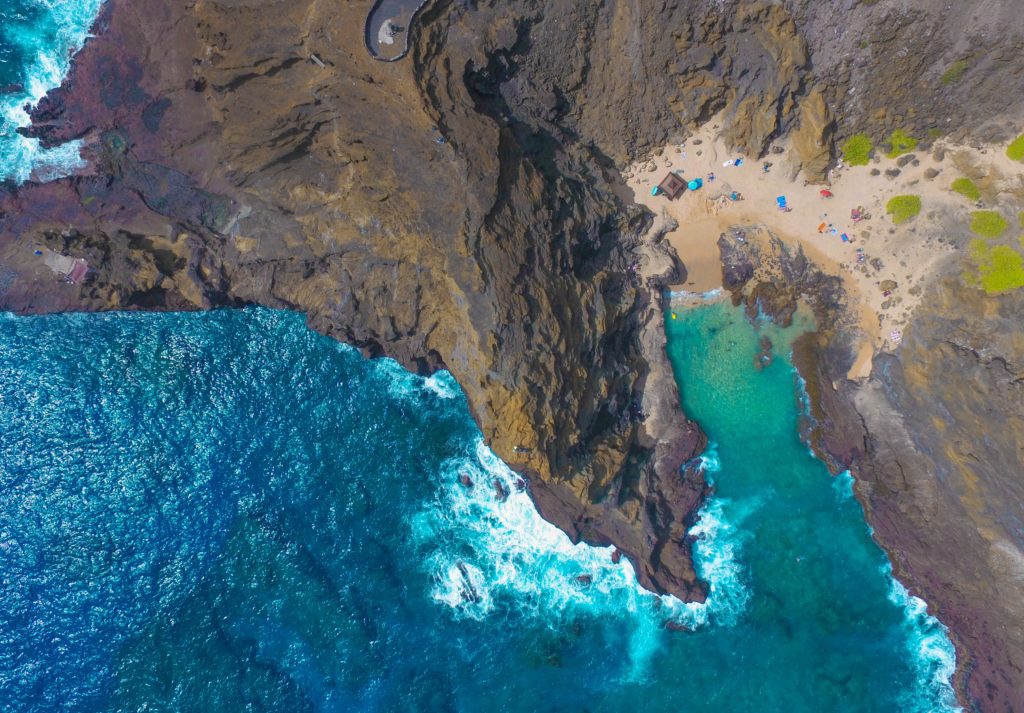 An aerial landscape of a hidden beach in Honolulu, Hawaii with bright turquoise water and rocky cliffs. This image is featured in the travel blog by Students Fare, "Best Destinations for Group Vacations," which lists the top locations for youth and student groups to travel!