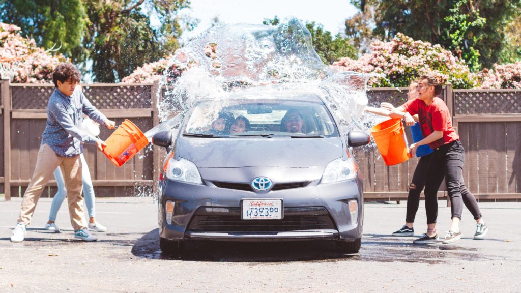 This image of a student group throwing buckets of water onto a car getting a fundraising car wash is featured in the Students Fare travel blog, "Fundraising Ideas for Students," which describes different fundraisers for students and faculty to fund study abroad programs and school trips.
