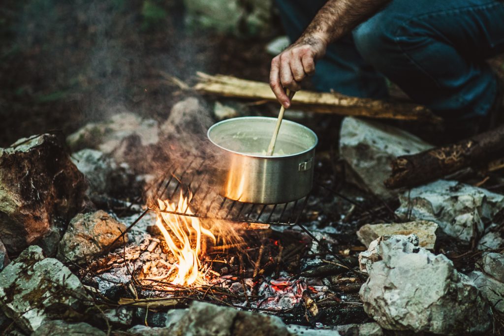 Featured in Backpacking Guide for Students by Students Fare, this image shows a campfire with a pot of boiling water over it.