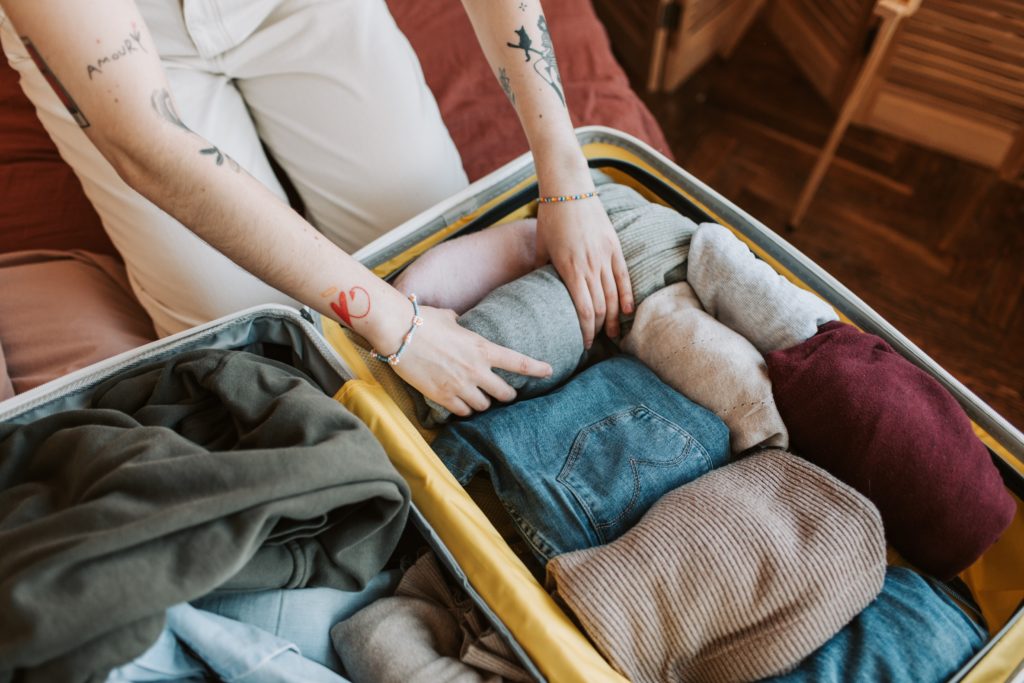 Featured in Packing for Study Abroad by Students Fare, this image shows a suitcase full of clothes and someone ready to do educational travel.