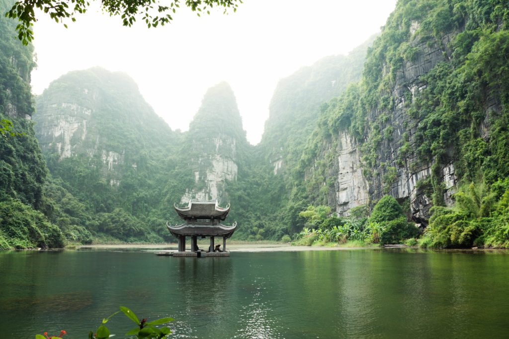 Featured in Affordable Vacation Destinations by Students Fare, this image shows a temple surrounded by a lake and mountains in Vietnam.