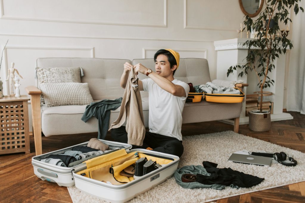 Featured in Students Fare's blog article "Packing Tips for Student Travelers," this image shows an Asian male folding clothes to pack into his yellow suitcase for a study abroad.