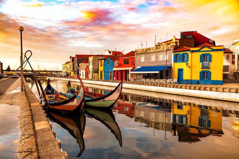 Aveiro, Portugal, Traditional colorful Moliceiro boats docked in the water canal among historical buildings during sunset.