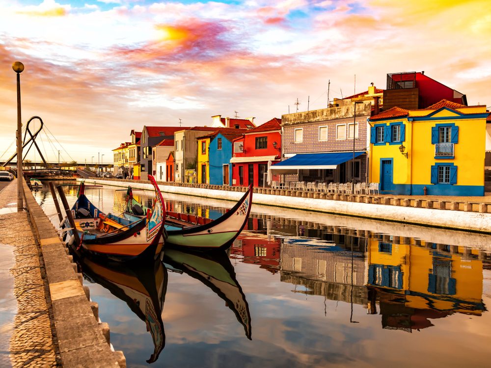 Aveiro, Portugal, Traditional colorful Moliceiro boats docked in the water canal among historical buildings during sunset.